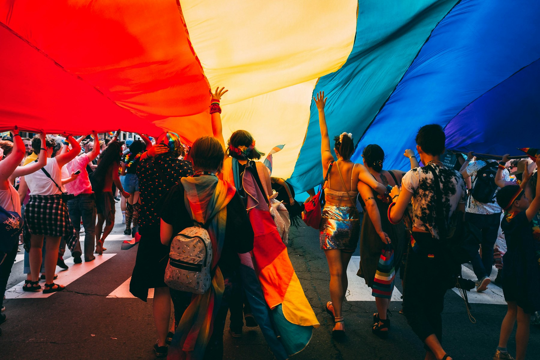 Pride parade marching under a giant rainbow flag